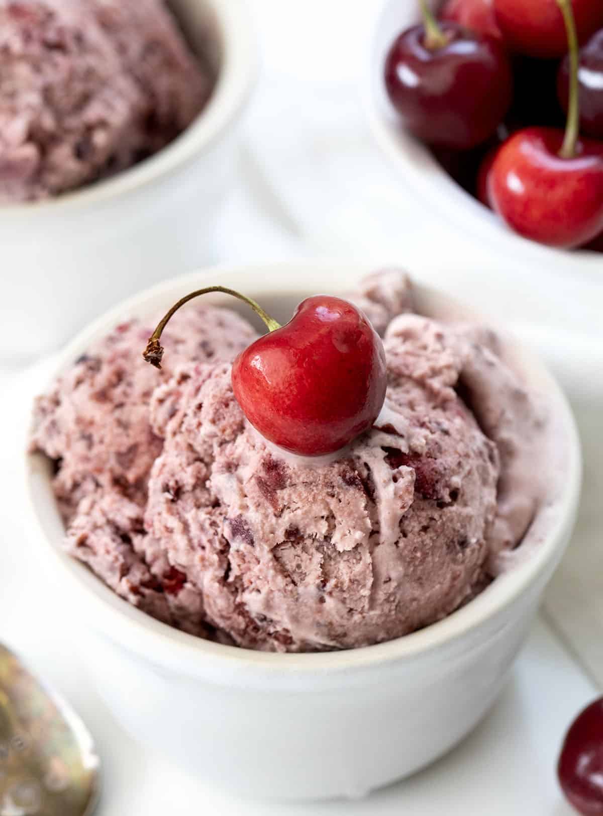 Bowls of Cherry No Churn Ice Cream on a white table with fresh cherries.