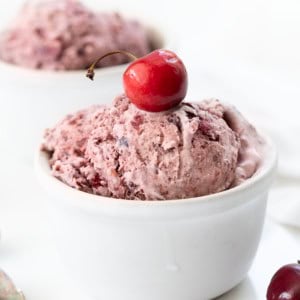 White bowls of Cherry No Churn Ice Cream on a white table with fresh cherries.