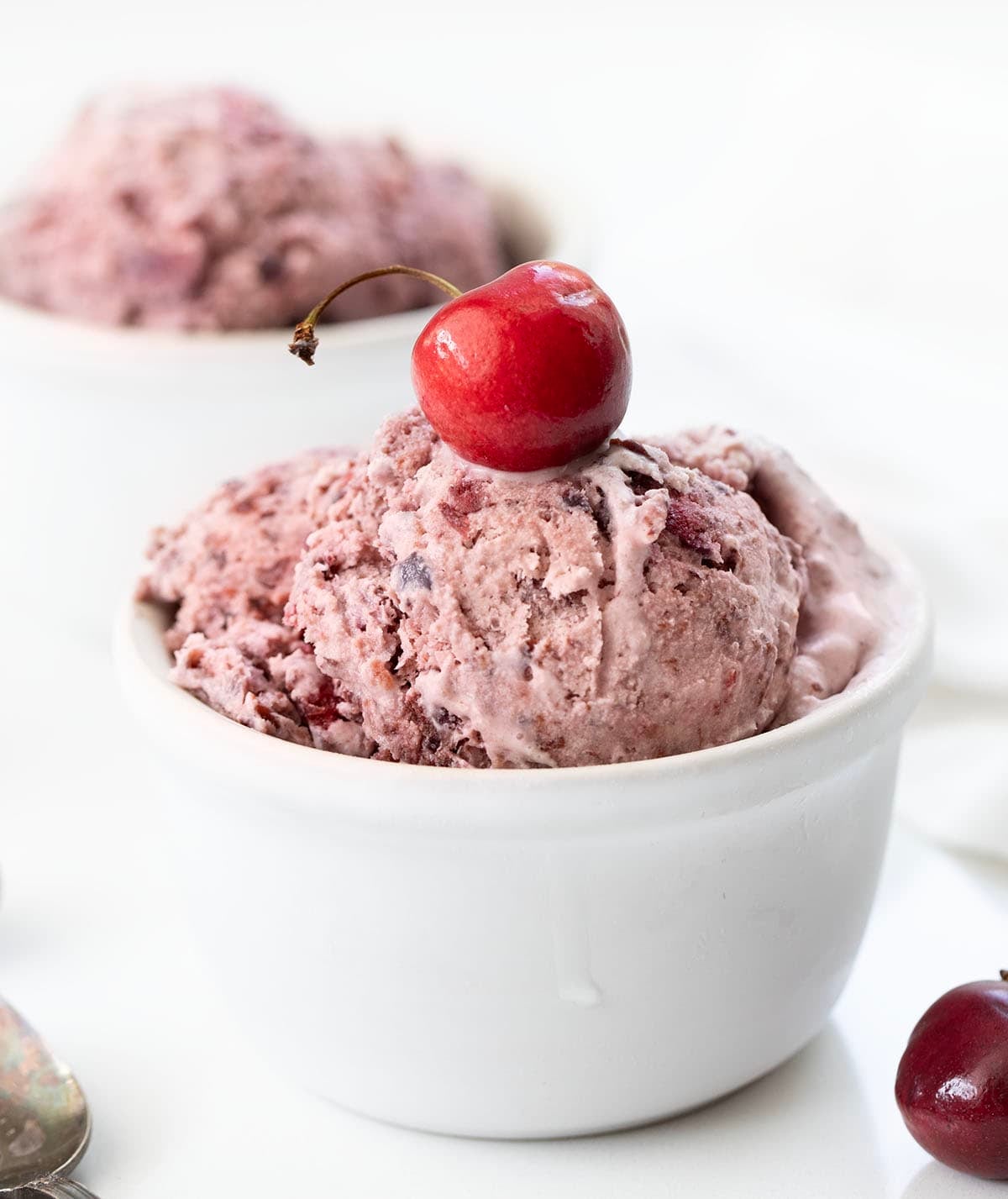 White bowls of Cherry No Churn Ice Cream on a white table with fresh cherries.