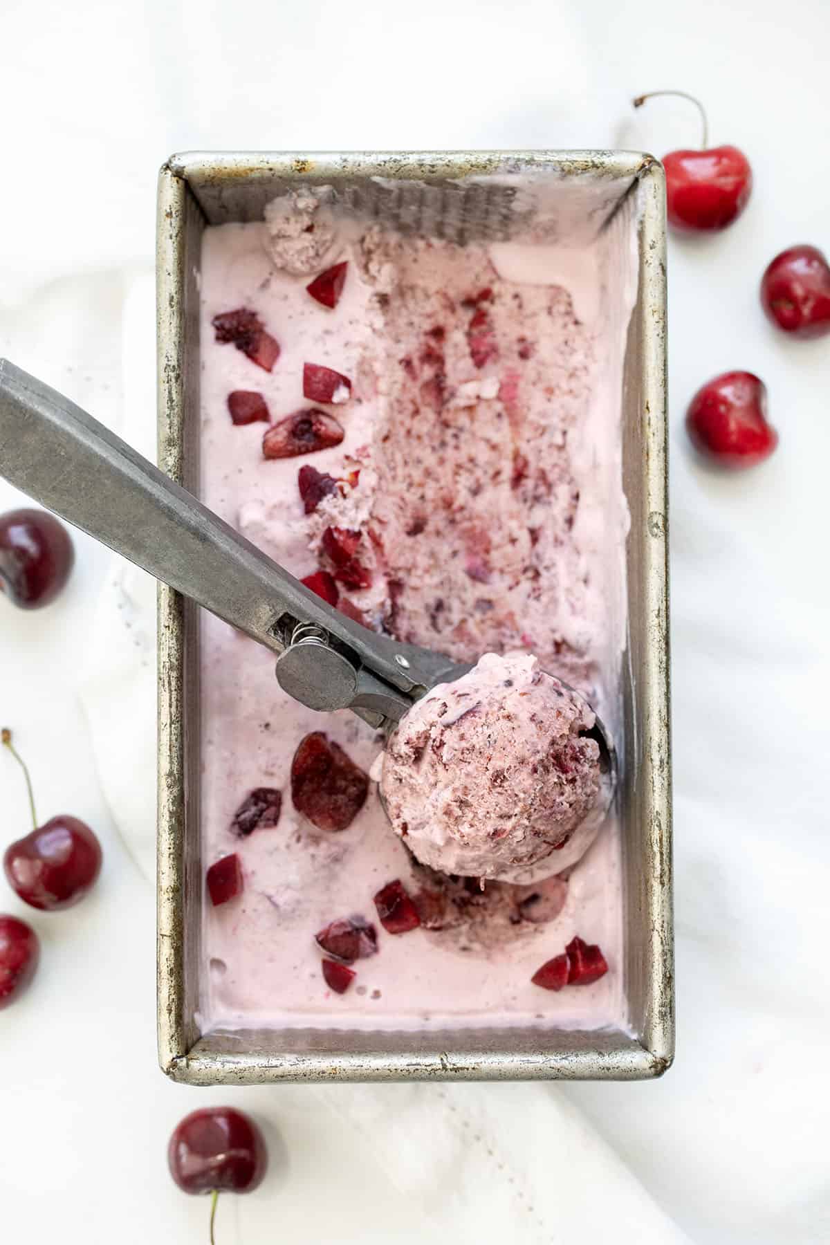 Pan of Cherry No Churn Ice Cream on a white table with an ice cream scooper filled.