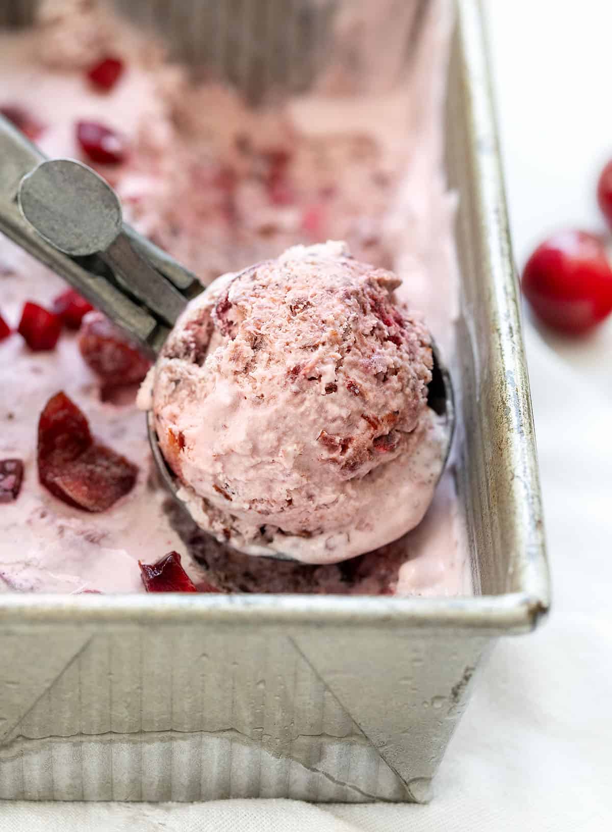 Close up of a filled scoop of Cherry No Churn Ice Cream in the pan.