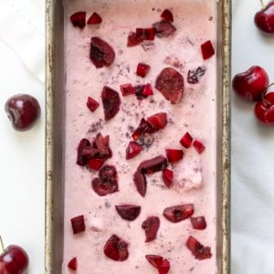 Pan of Cherry No Churn Ice Cream on a white table with fresh cherries.
