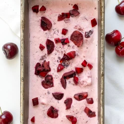 Pan of Cherry No Churn Ice Cream on a white table with fresh cherries.