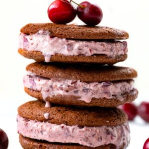 Stack of Chocolate Cherry Ice Cream Sandwiches on a white table with fresh cherries.