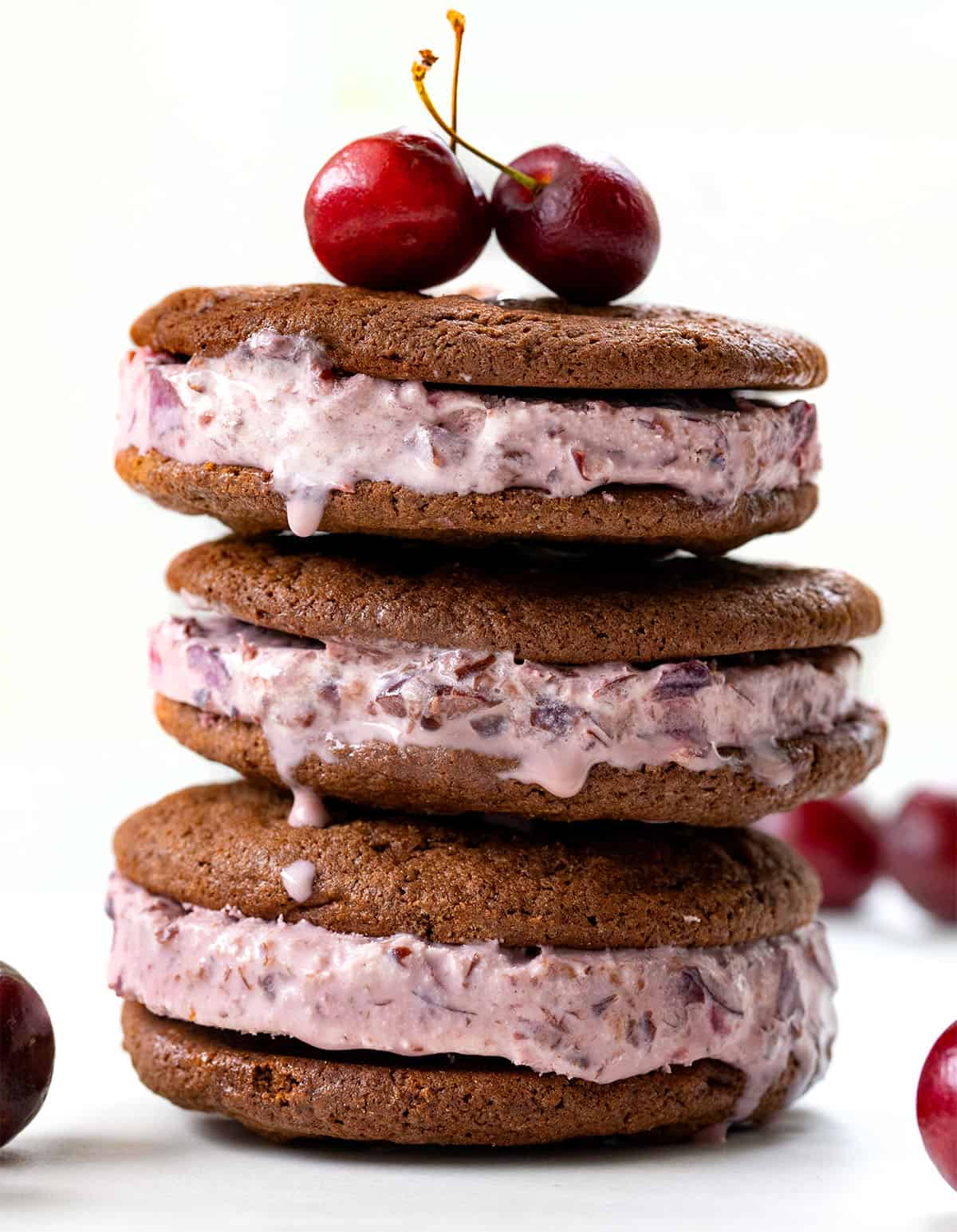 Stack of Chocolate Cherry Ice Cream Sandwiches on a white table with fresh cherries.