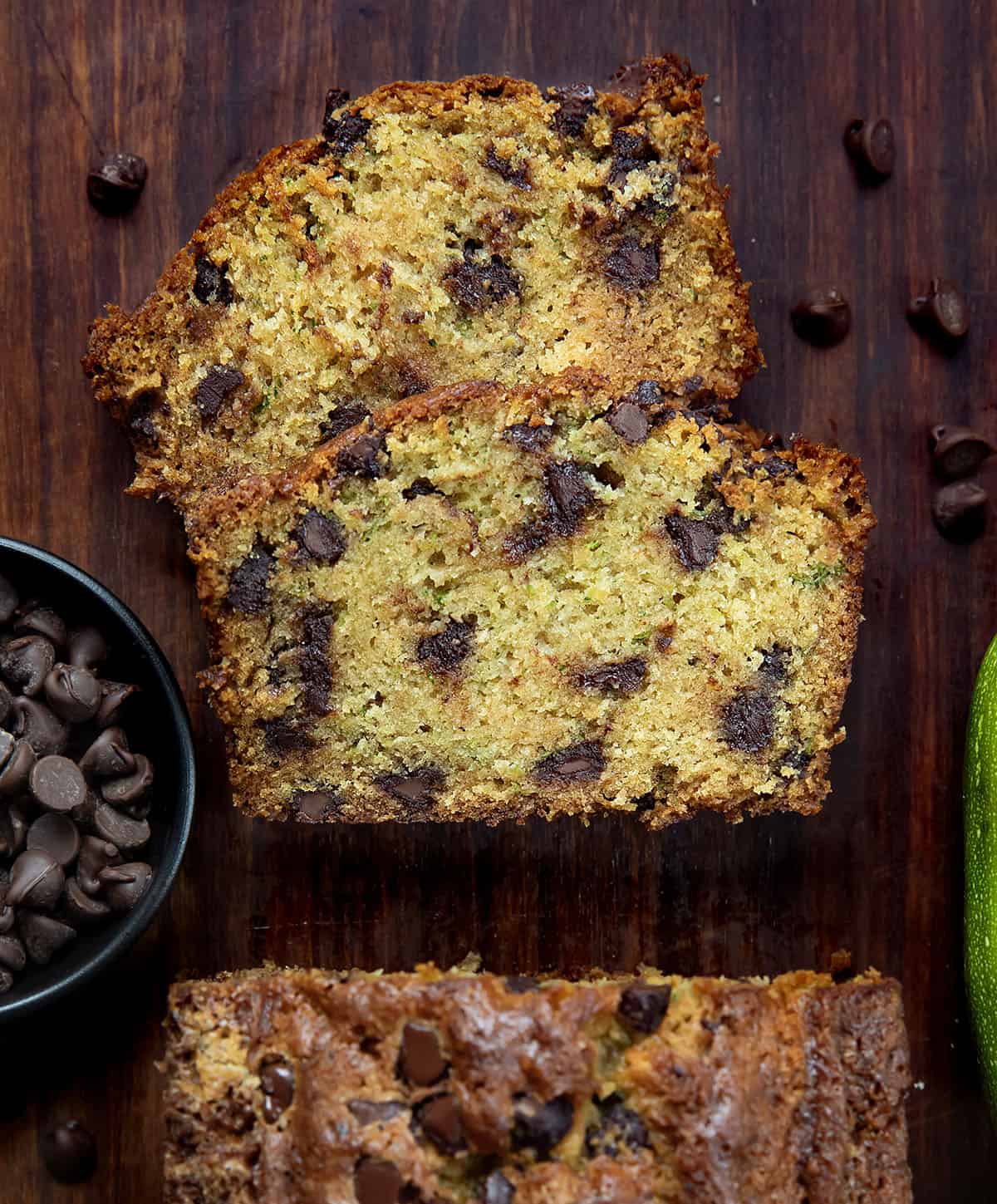 Loaf of Chocolate Chip Zucchini Bread one a wooden table from overhead with a couple of slices laying flat on the table.