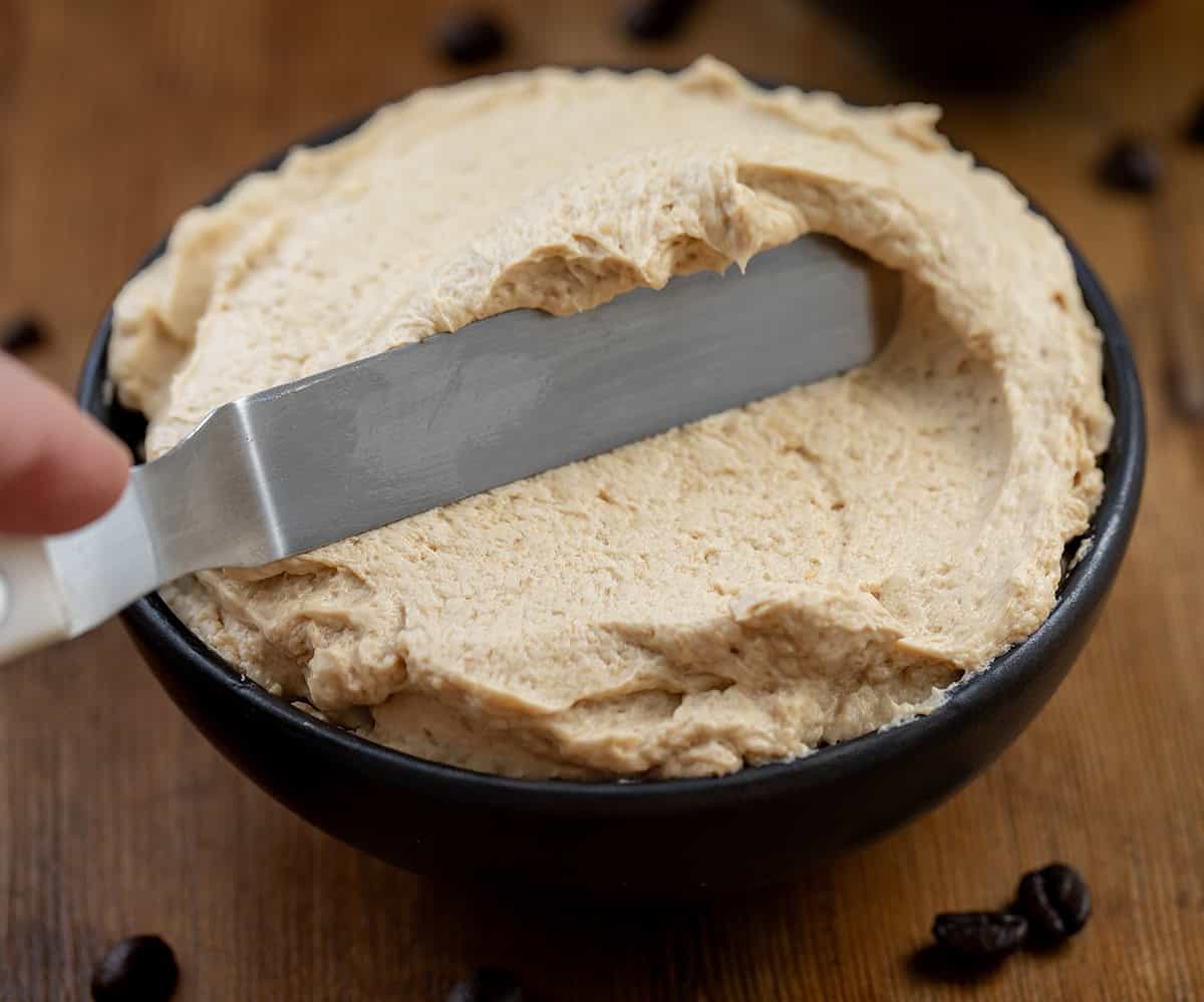 Using a spatula to spread frosting around a black bowl.