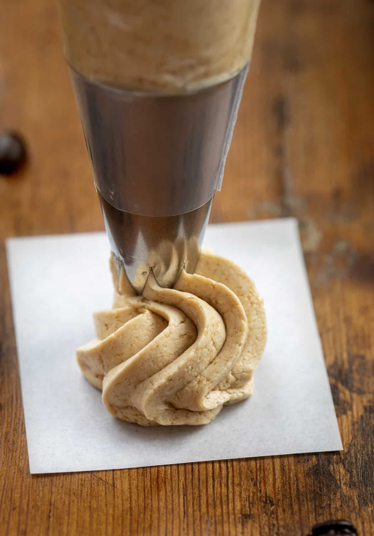 Piping a dollop of Espresso Ermine onto a piece of parchment paper on a wooden table.