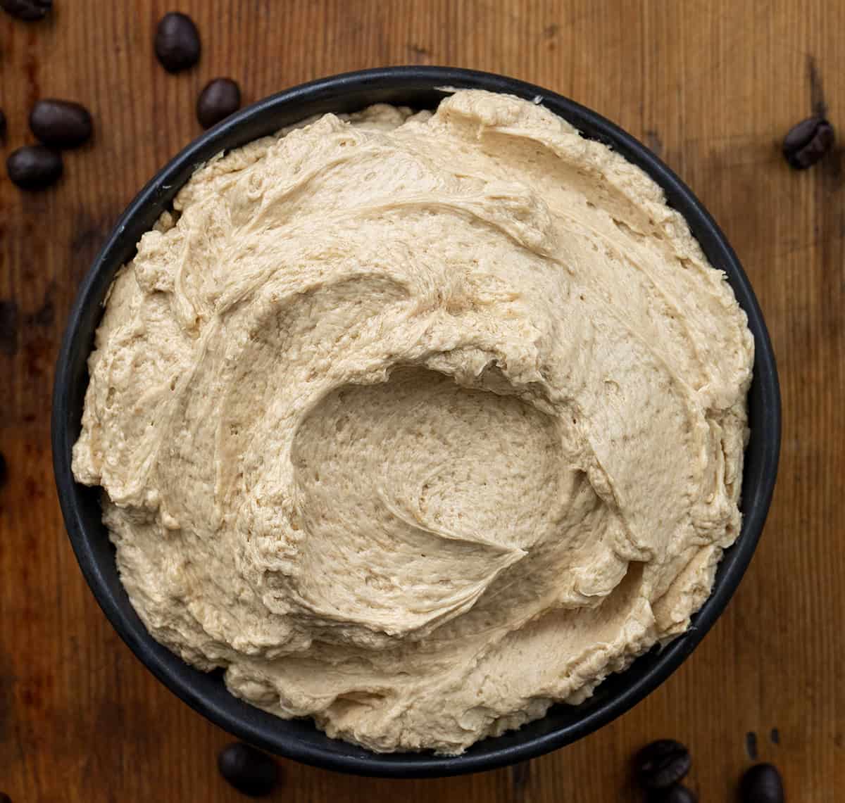 Black bowl filled with Espresso Ermine frosting on a wooden table from overhead.