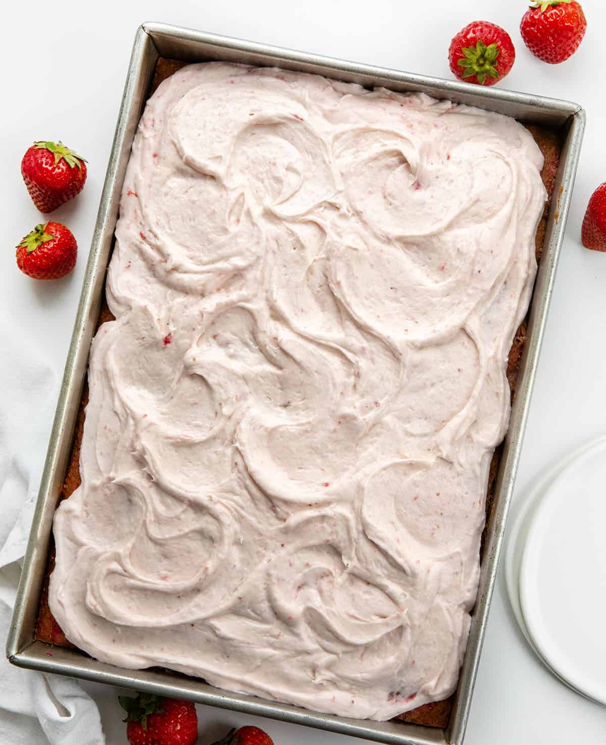 Strawberry Sheet Cake with Strawberry Cream Cheese Frosting on a white table with strawberries from overhead.
