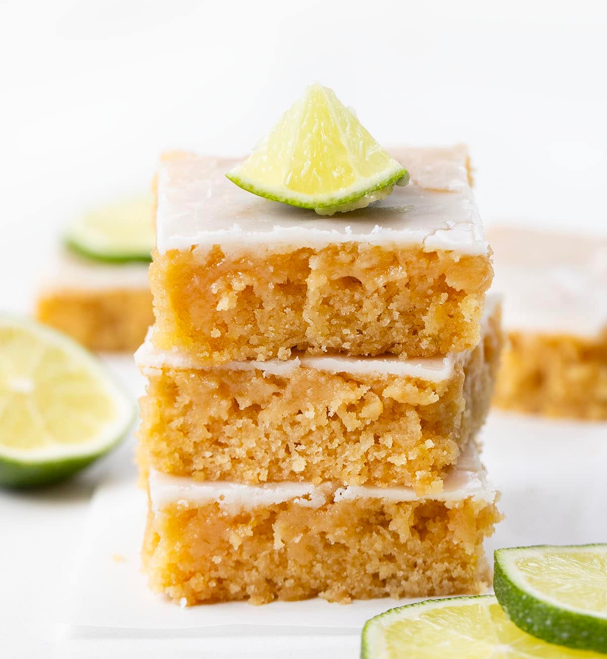 Stack of Lime Brownies on a white table with fresh cut limes.
