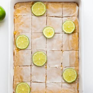 Pan of Lime Brownies cut into squares with lime slices on a white table from overhead.