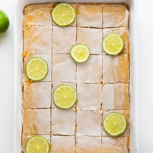 Pan of Lime Brownies cut into squares with lime slices on a white table from overhead.