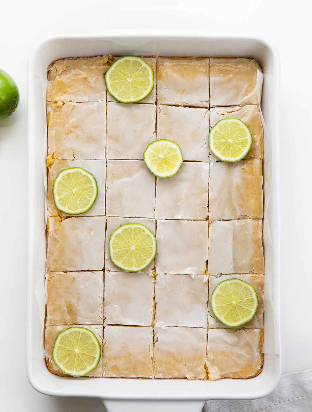 Pan of Lime Brownies cut into squares with lime slices on a white table from overhead.