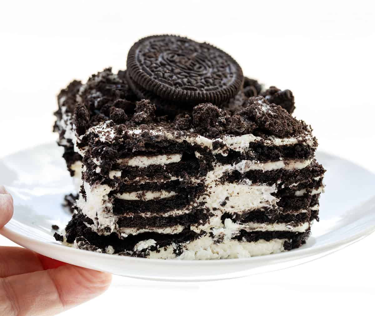 Hand holding a white plate with Oreo Icebox Cake on it.