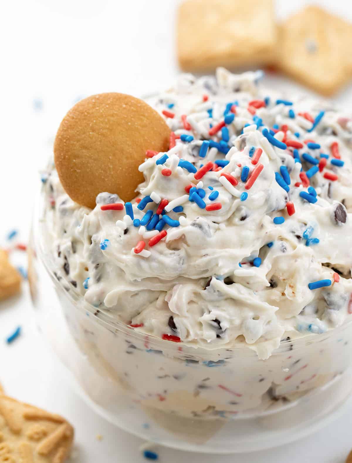 Glass bowl filled with Patriotic Booty Dip, or Patriotic Chocolate Chip Dip, and a vanilla wafer in the dip.