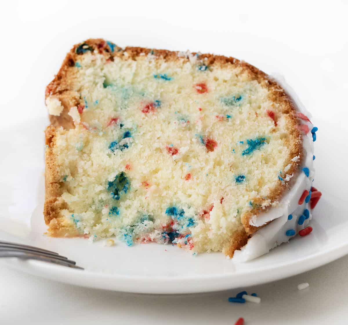 Piece of Red, White, and Blue Pound Cake on a white plate with a bite removed.