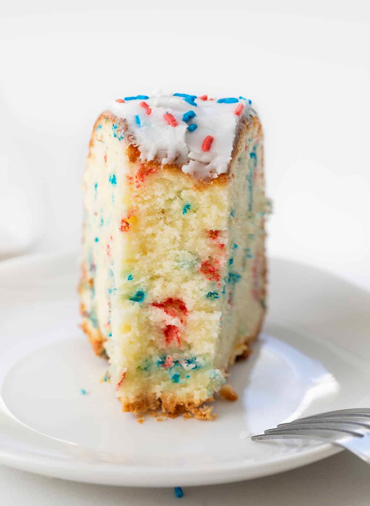 Piece of Red, White, and Blue Pound Cake on a white plate with a bite removed.