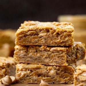 Stack of Peanut Butter Overload Blondies on a wooden table with peanut butter.