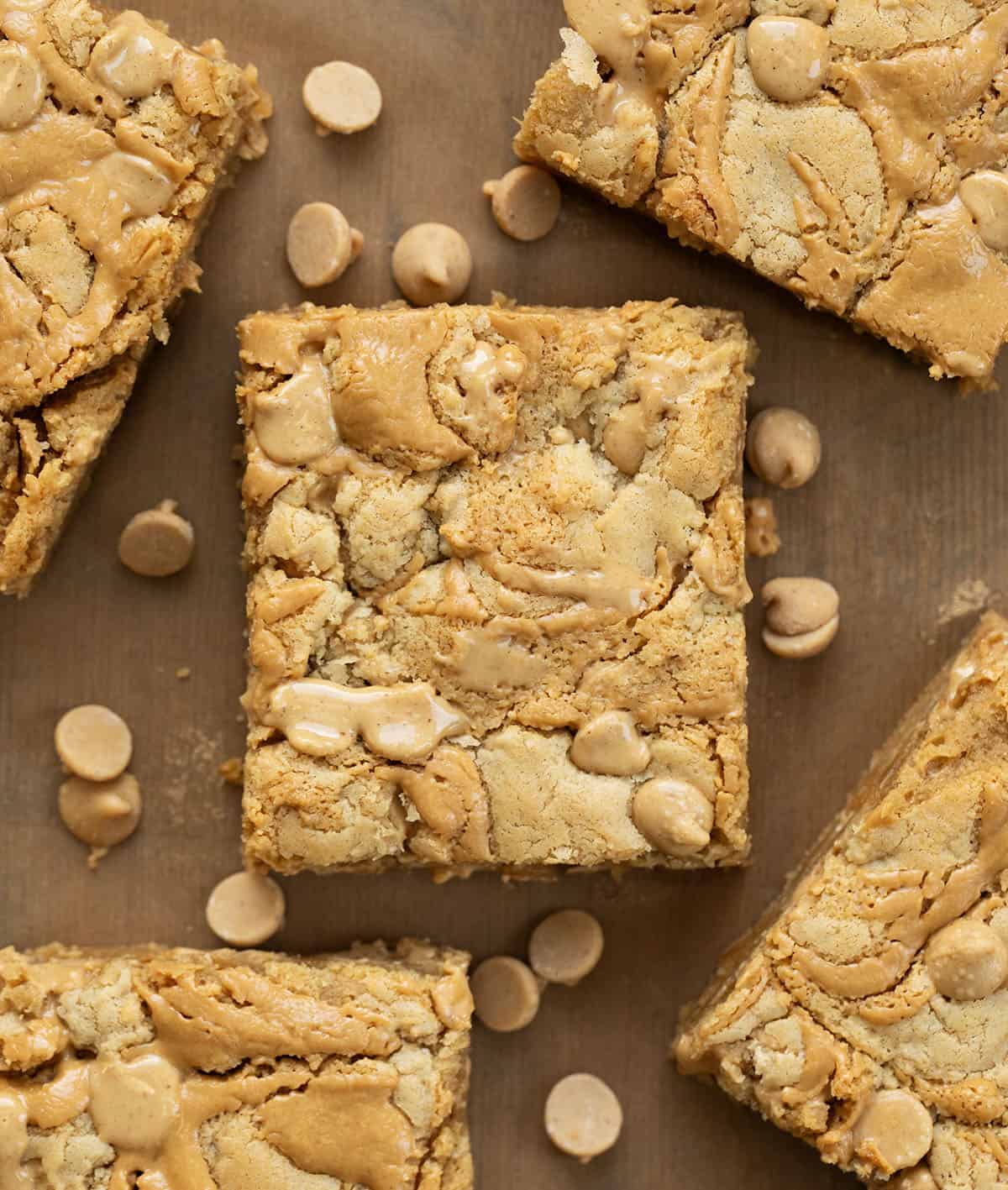 Peanut Butter Overload Blondies cut into squares on a wooden table with tan parchment from overhead.