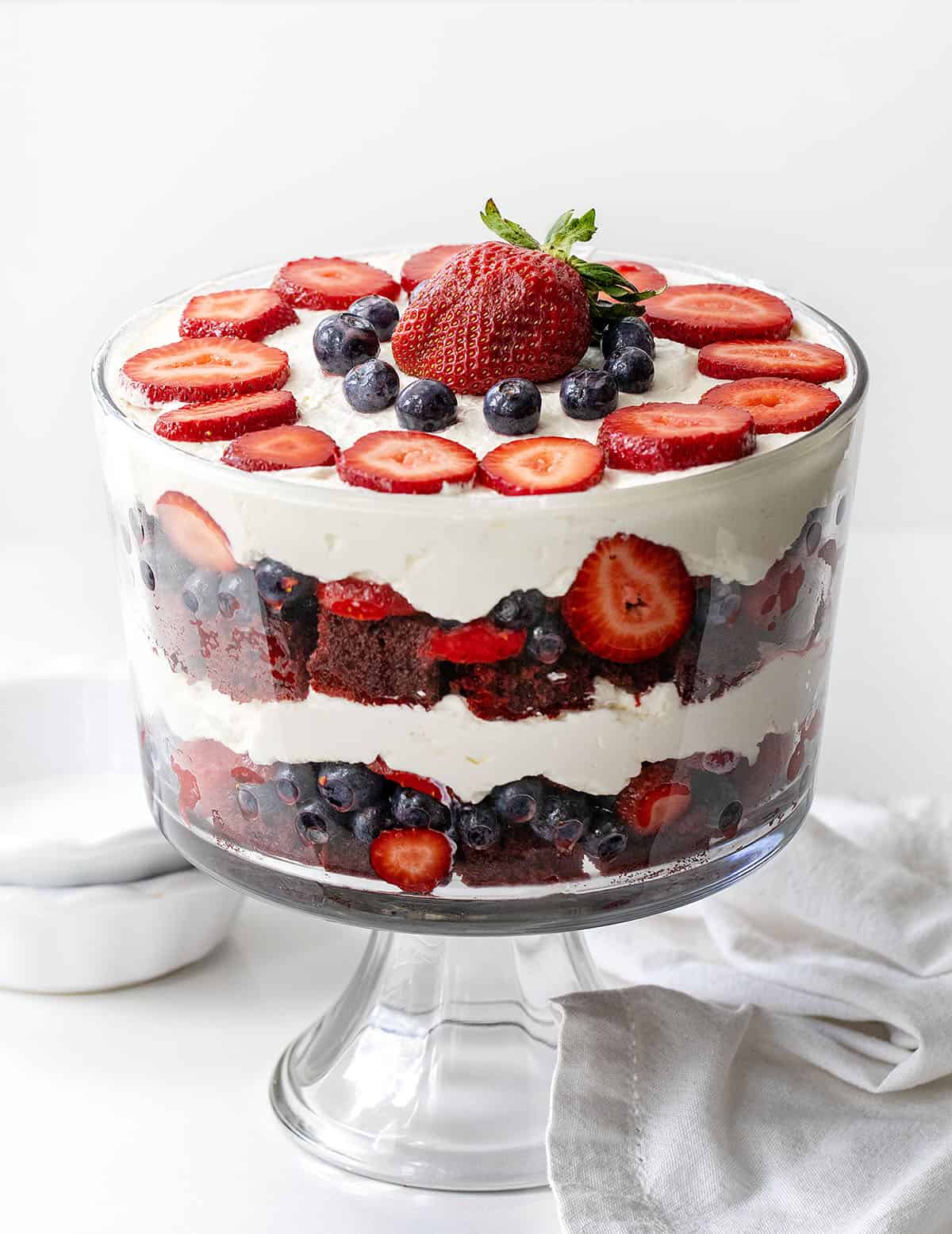 Layered Red Velvet Berry Trifle with Fresh Berries and Whipped Cream Red Velvet Berry Trifle on a white table with white towel and dishes.