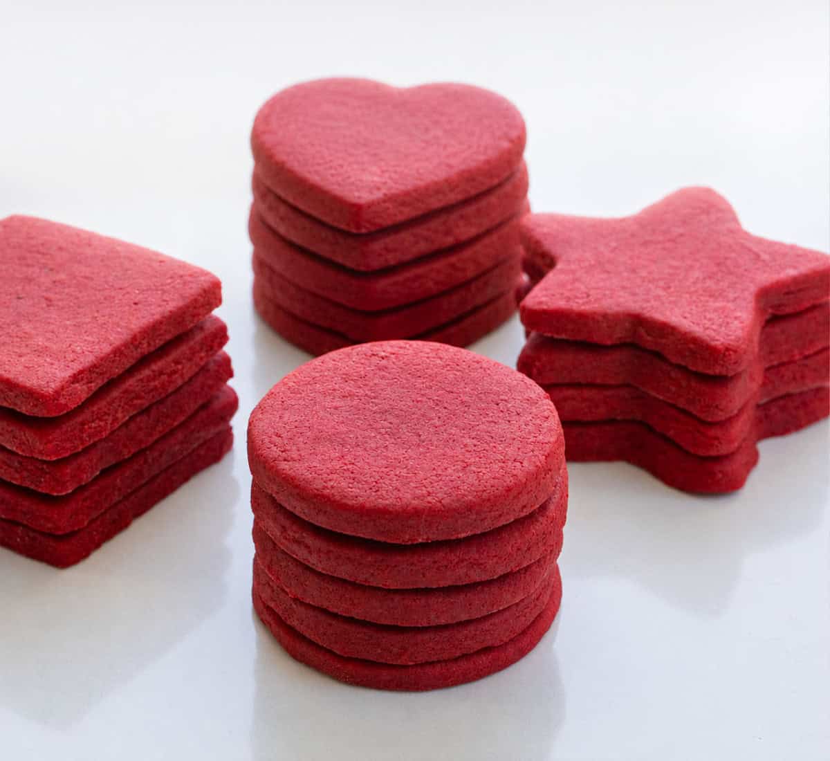 Stacks of Red Velvet Cut-Out Sugar Cookies on a white table.