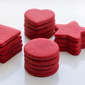 Stacks of Red Velvet Cut-Out Sugar Cookies on a white table.