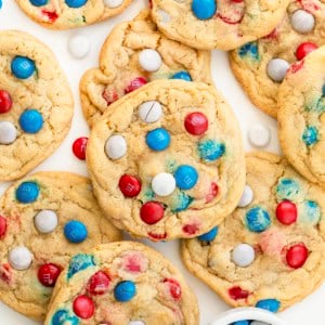 Close up of Red, White, and Blue M&M Cookies on a white table with a white bowl of M&M's next to the cookies.