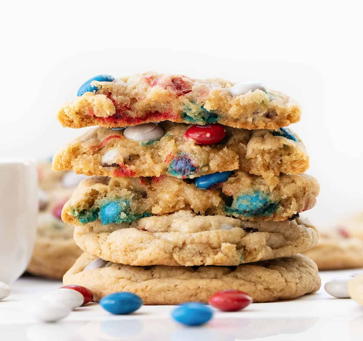 Small stack of Red, White, and Blue M&M Cookies with the top cookies broken in half showing the soft texture inside.
