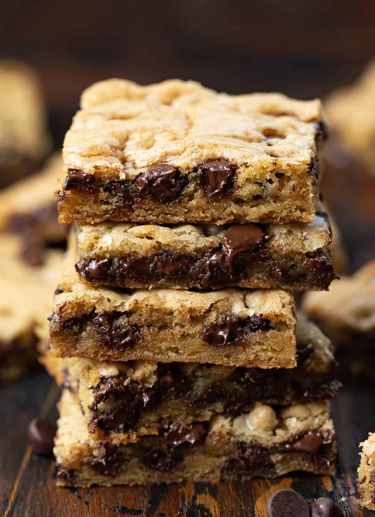 These Sheet Pan Chocolate Chip Cookies are an easy way to make a big batch of soft, chewy chocolate chip cookies in one pan. Thick, buttery, and loaded with chocolate chips, they bake up golden on the edges with a soft center in every bite. Stack of Sheet Pan Chocolate Chip Cookies on a wooden table surrounded by more sheet pan cookie bars.