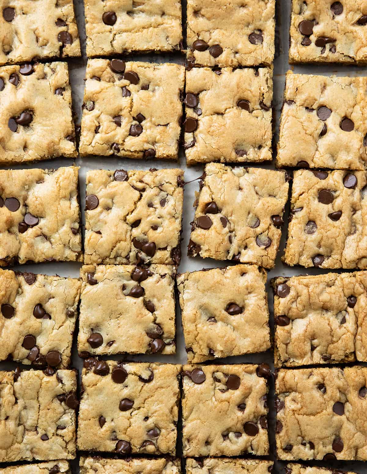 These Sheet Pan Chocolate Chip Cookies are an easy way to make a big batch of soft, chewy chocolate chip cookies in one pan. Thick, buttery, and loaded with chocolate chips, they bake up golden on the edges with a soft center in every bite. Sheet Pan Chocolate Chip Cookies cut into squares on tan parchment paper from overhead.