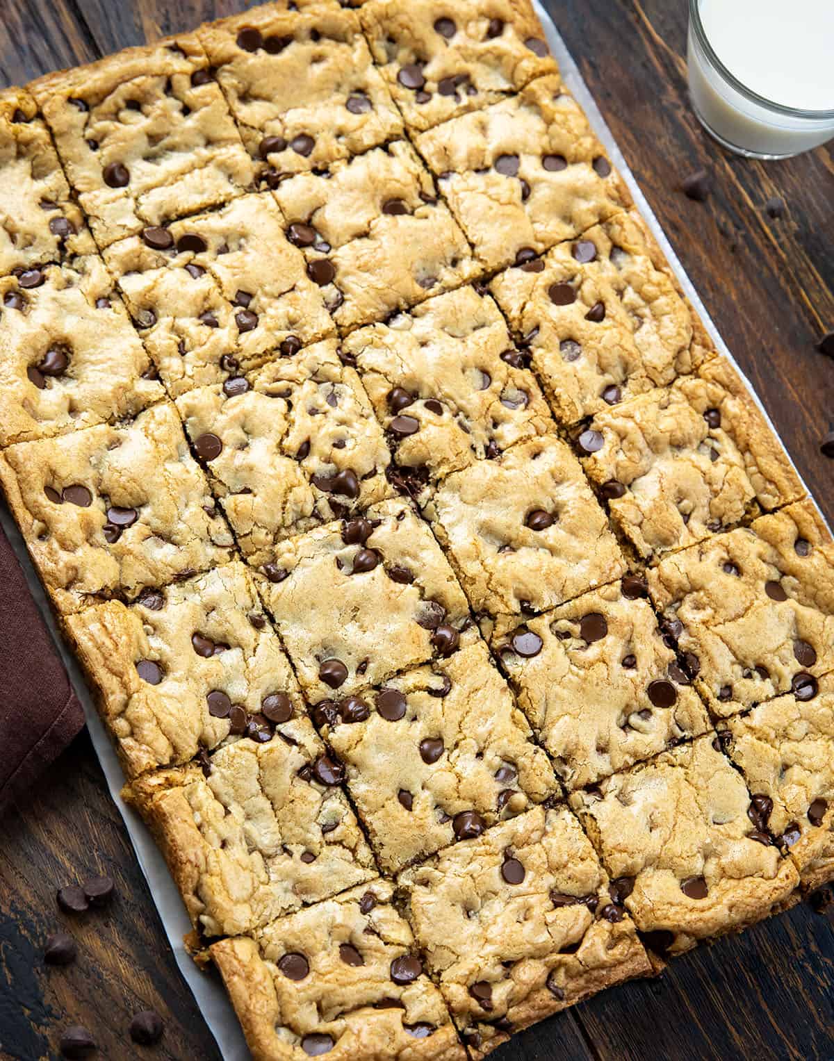 These Sheet Pan Chocolate Chip Cookies are an easy way to make a big batch of soft, chewy chocolate chip cookies in one pan. Thick, buttery, and loaded with chocolate chips, they bake up golden on the edges with a soft center in every bite. Sheet Pan Chocolate Chip Cookies on a wooden table with glass of milk.