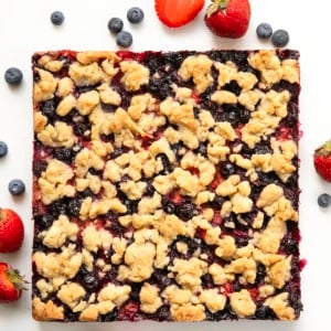 Strawberry Blueberry Crumble Bars fresh from the oven on a white table with fresh blueberries and strawberries.