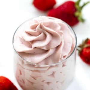 Piped Strawberry Stabilized Whipped Cream in a glass with fresh strawberries around it.