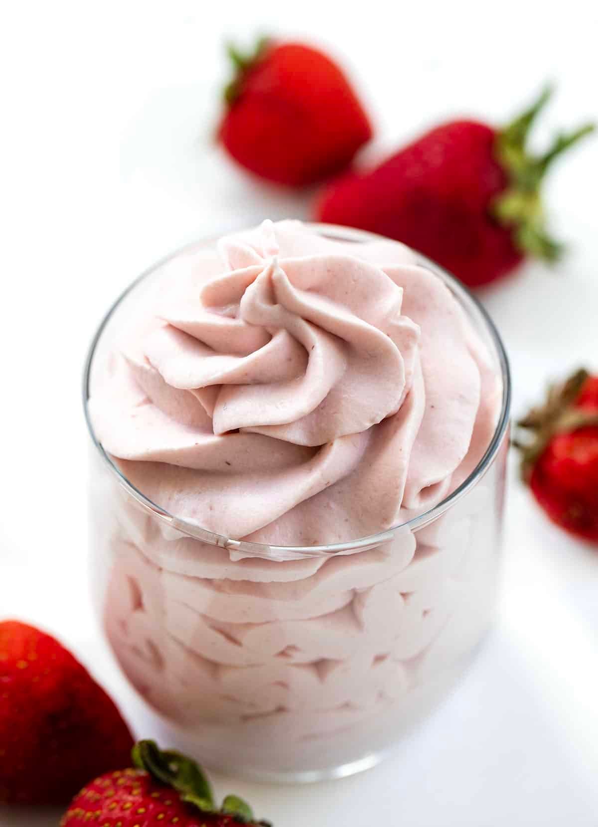 Piped Strawberry Stabilized Whipped Cream in a glass with fresh strawberries around it.