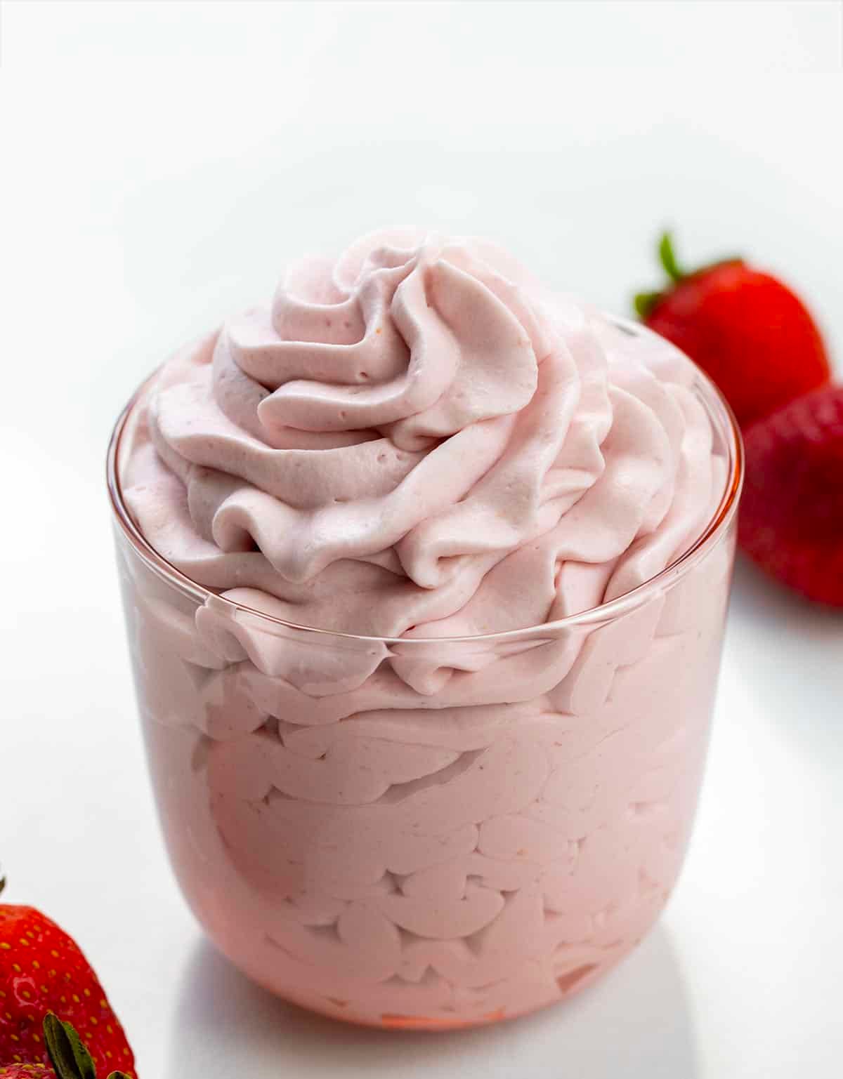 Strawberry Stabilized Whipped Cream in a pink glass on a white table with strawberries.