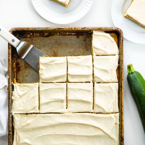 Pan of Zucchini Bars covered in cream cheese frosting and some of the bars are removed and some are cut in the pan.