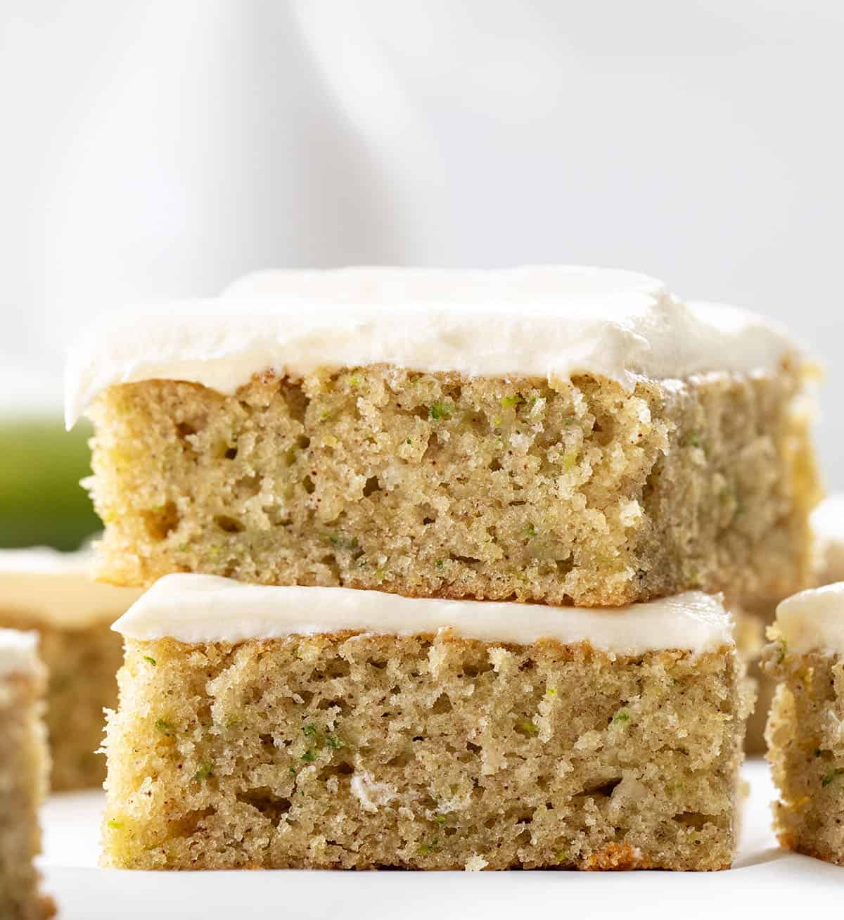 Close up of a stack of two Zucchini Bars with zucchini in the background.