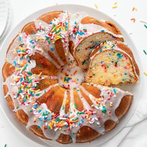 Birthday Pound Cake on a white platter with a couple of pieces cut and laying so that the texture of the cake is visible.