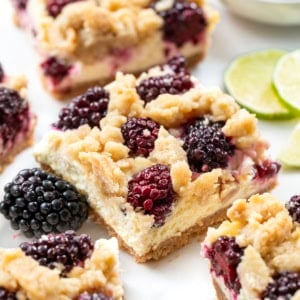 Close up of Blackberry Lime Cheesecake Bar surrounded by limes and blackberries.