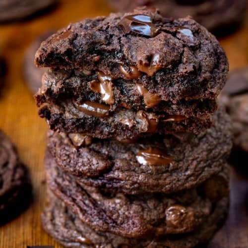 Close up of stack of Bloomed Cocoa Chocolate Chip Cookies with top cookies broken in half showing melted chocolate chips.