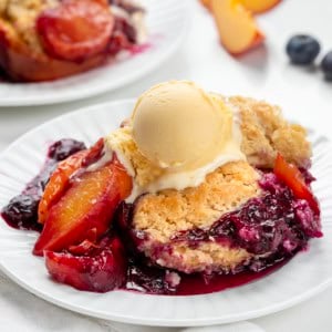 White plates of Blueberry Peach Cobbler on a white table.