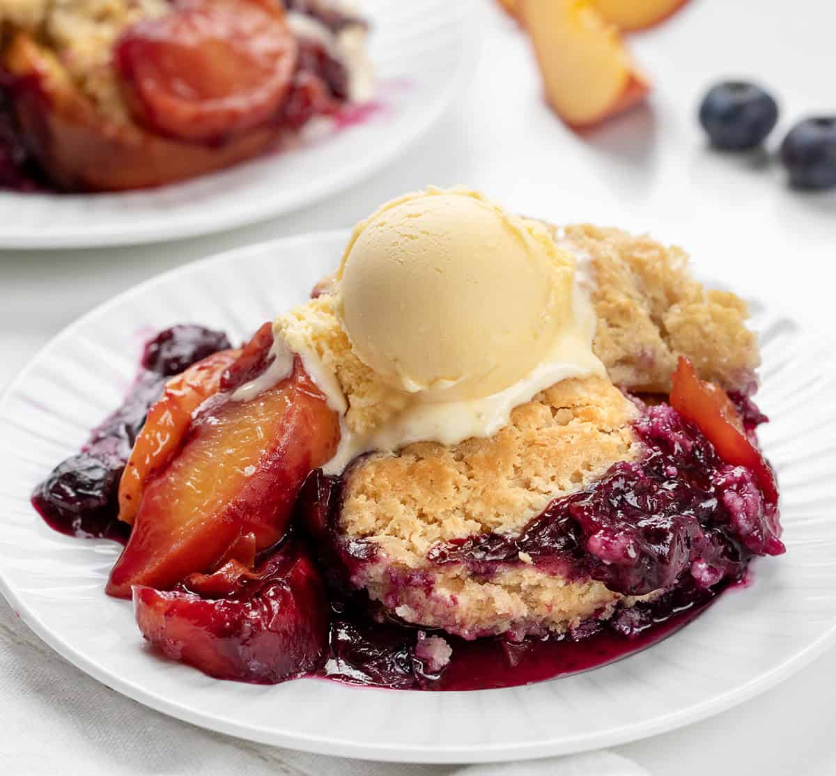 White plates of Blueberry Peach Cobbler on a white table.