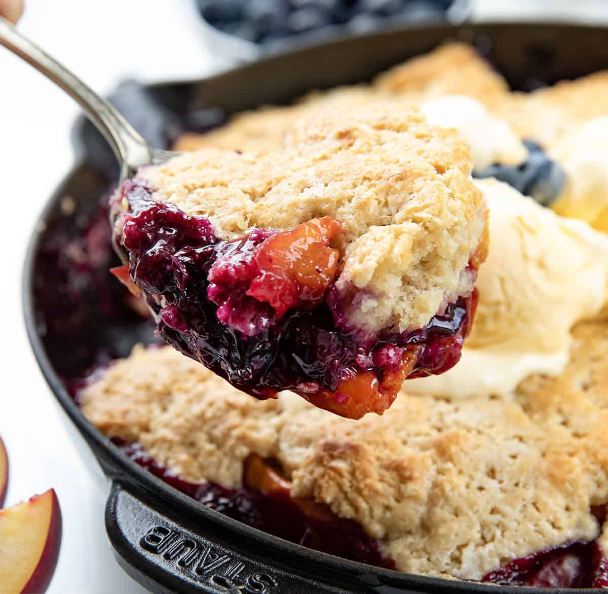 Spoonful of Blueberry Peach Cobbler being held above the skillet.