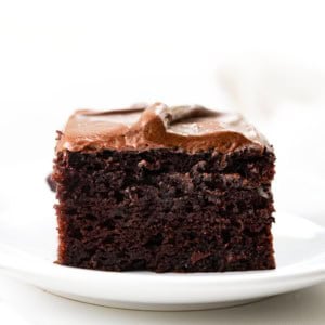 Slice of Chocolate Zucchini Snack Cake on a white plate on a white table.