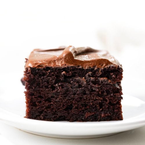Slice of Chocolate Zucchini Snack Cake on a white plate on a white table.