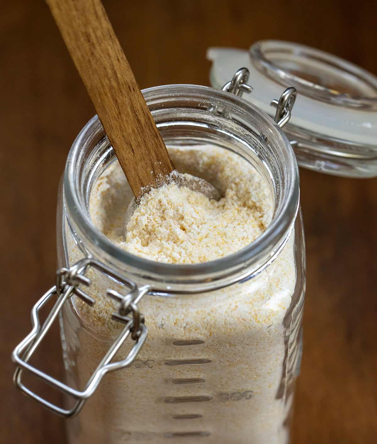 Glass jar of Homemade Cornbread Mix with a wooden measuring spoon in it.