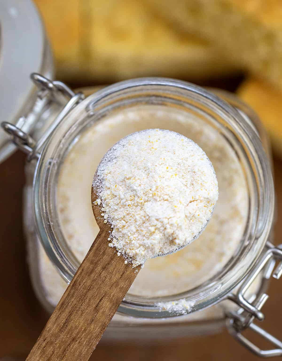 Full measuring spoon of Homemade Cornbread Mix held above the jar.