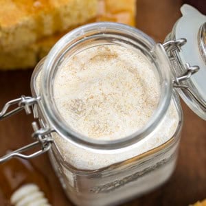 Close up on the open jar of Homemade Cornbread Mix on a wooden table with cornbread and honey.