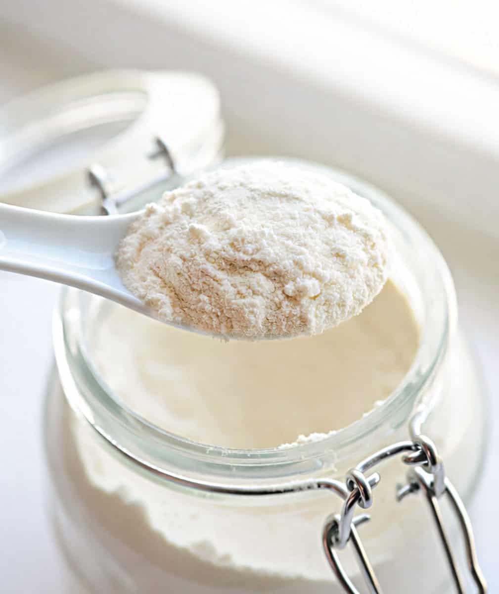 White spoon holding a spoonful of Homemade Vanilla Pudding Mix above the jar White spoon holding a spoonful of Homemade Vanilla Pudding Mix above the jar.